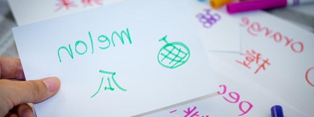 in the foreground a white index card with green wrting being held by a hand in front of other cards and markers.